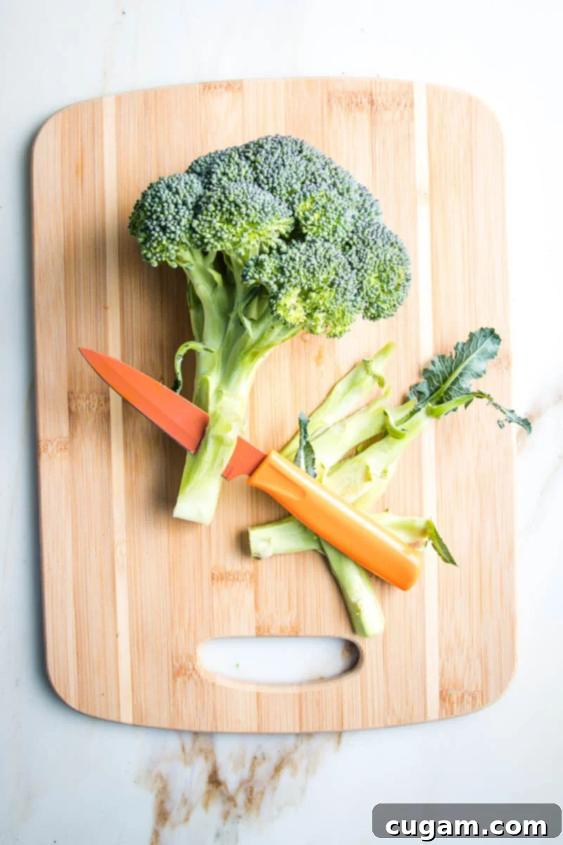 A paring knife expertly peeling off the tough, woody outer layer of a broccoli stalk, preparing it for roasting.