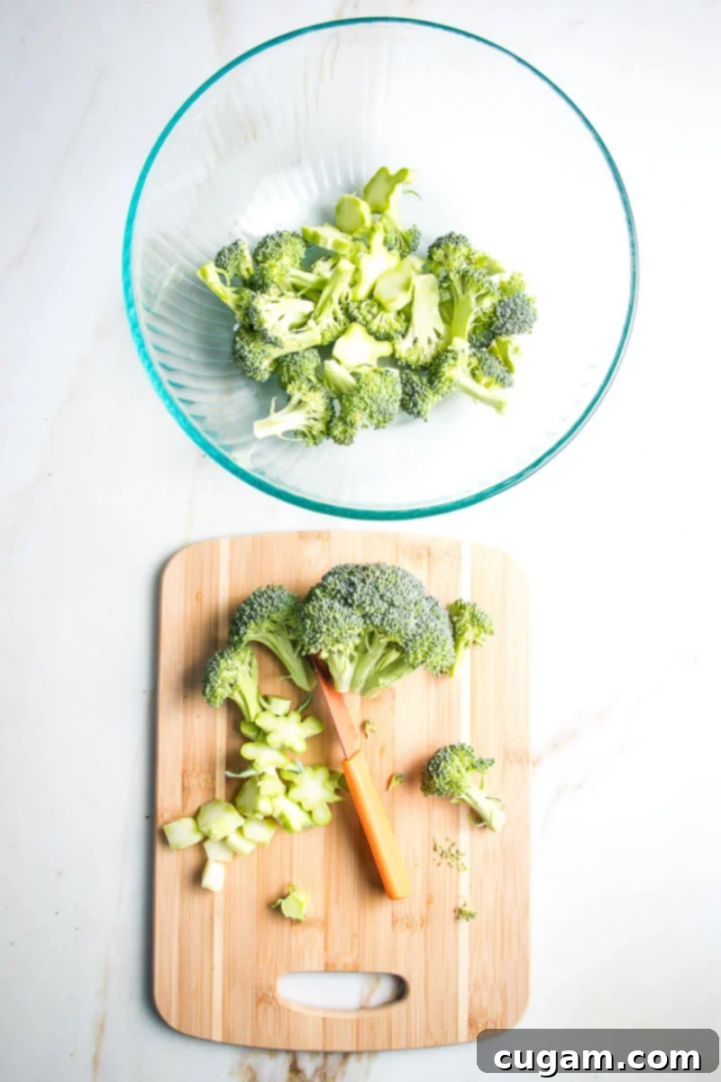 A large bowl filled with bite-sized pieces of fresh broccoli, including both florets and sliced stems, ready to be marinated for roasting.
