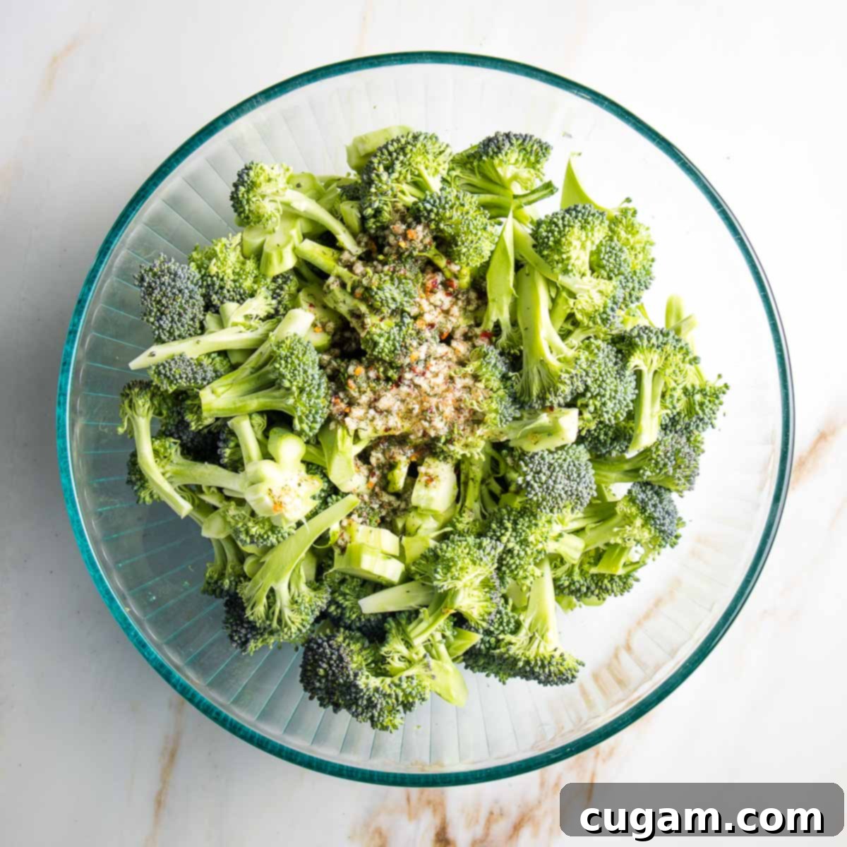 A large mixing bowl filled with fresh broccoli florets and stems, generously coated in a flavorful marinade, ready for roasting.