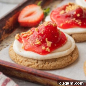 Baked strawberry cheesecake cookie on baking sheet with fresh strawberry.