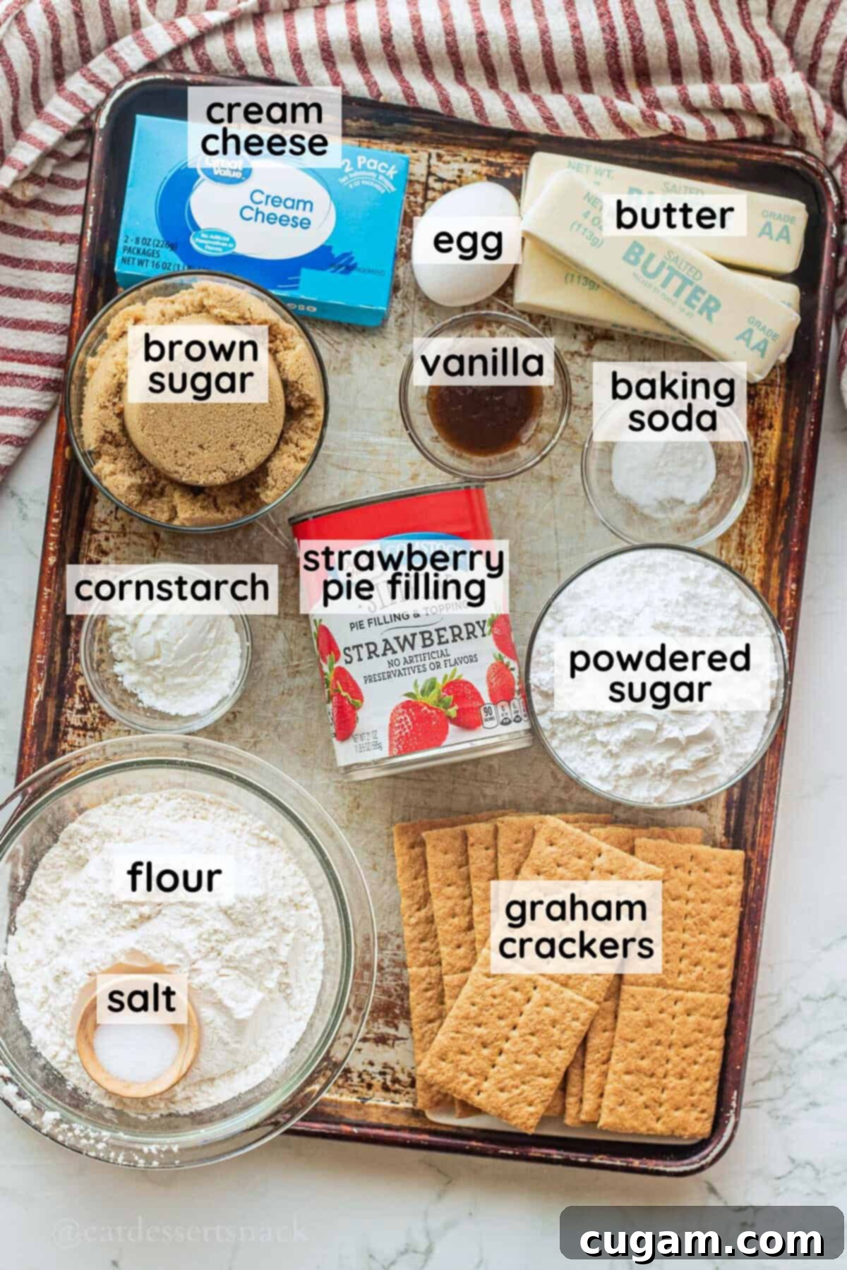 Labeled ingredients for strawberry cheesecake cookies in glass bowls on metal baking sheet.