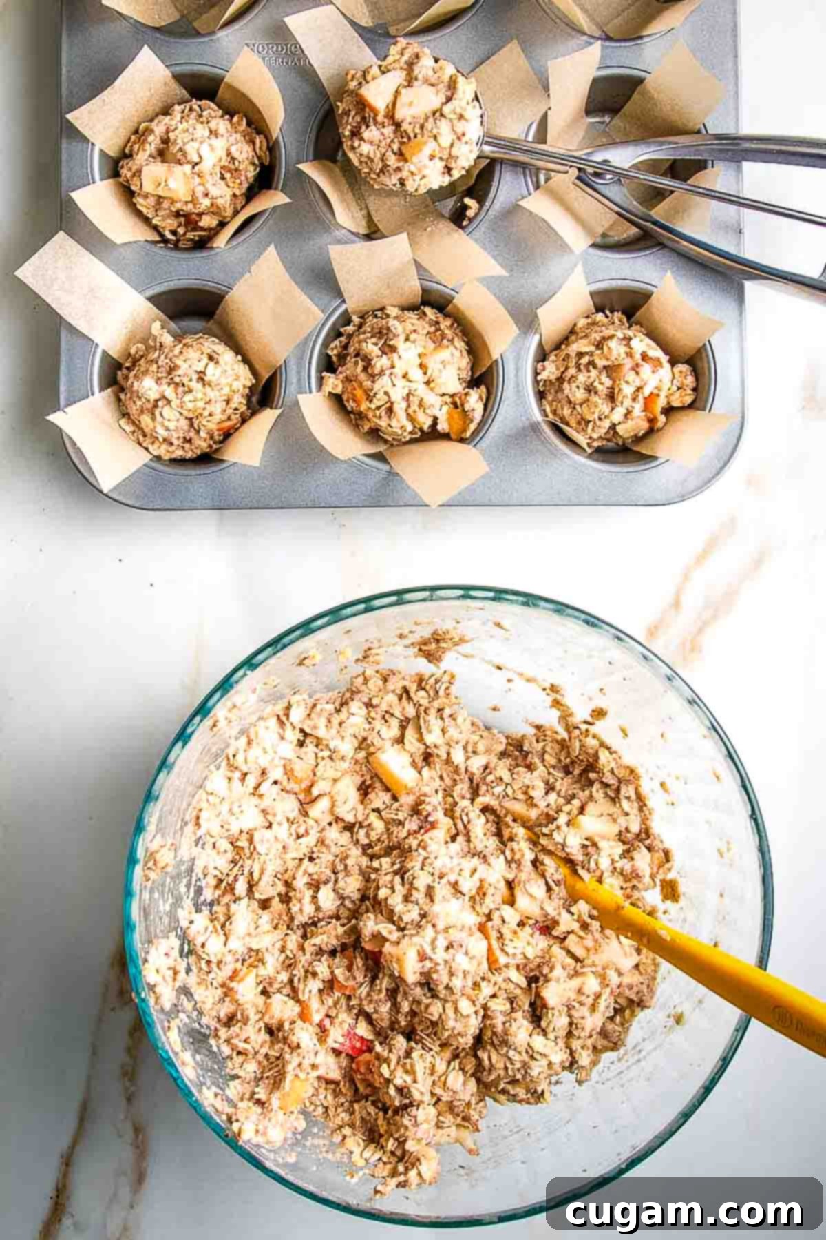 Using a small scoop to distribute muffin batter into prepared parchment-lined muffin tins.