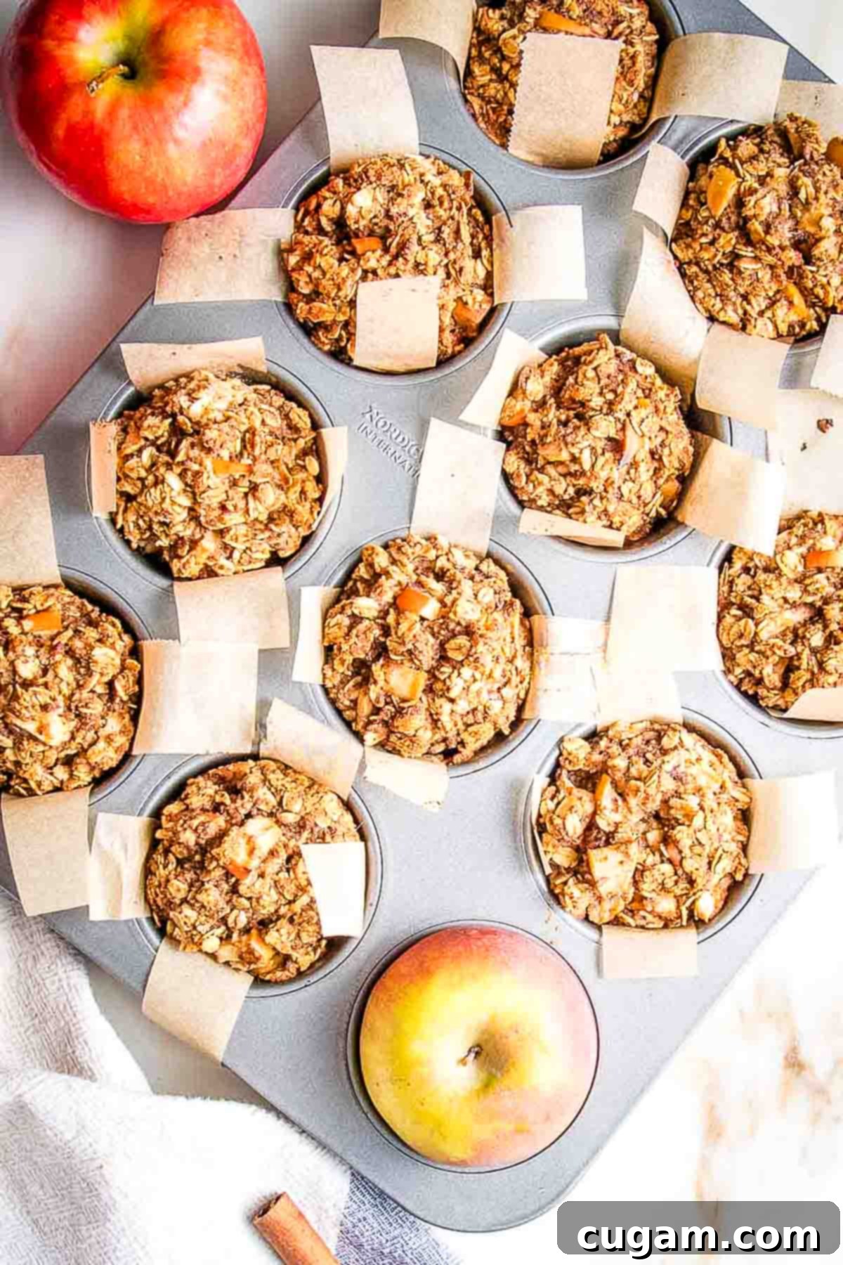 Golden brown oatmeal muffins with visible apple chunks, baked in a muffin tin.