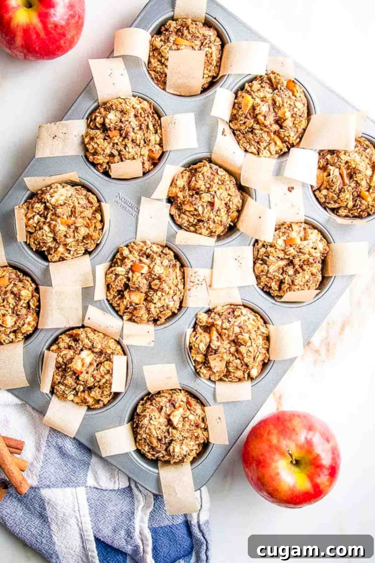 Close-up of baked oatmeal muffins with apple chunks, perfectly lined with parchment paper in a muffin tin.