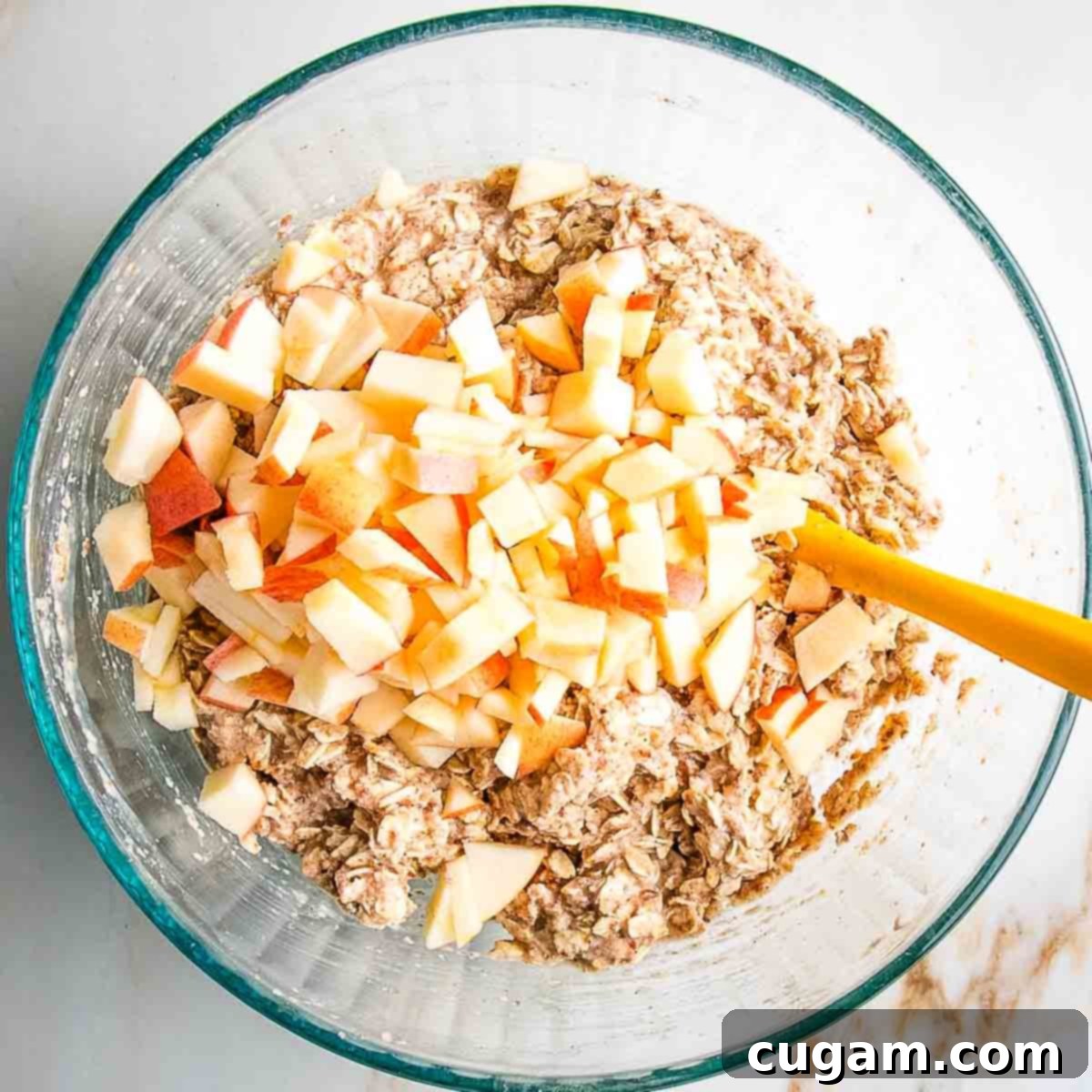 Stirring diced apples into the prepared oatmeal muffin batter.