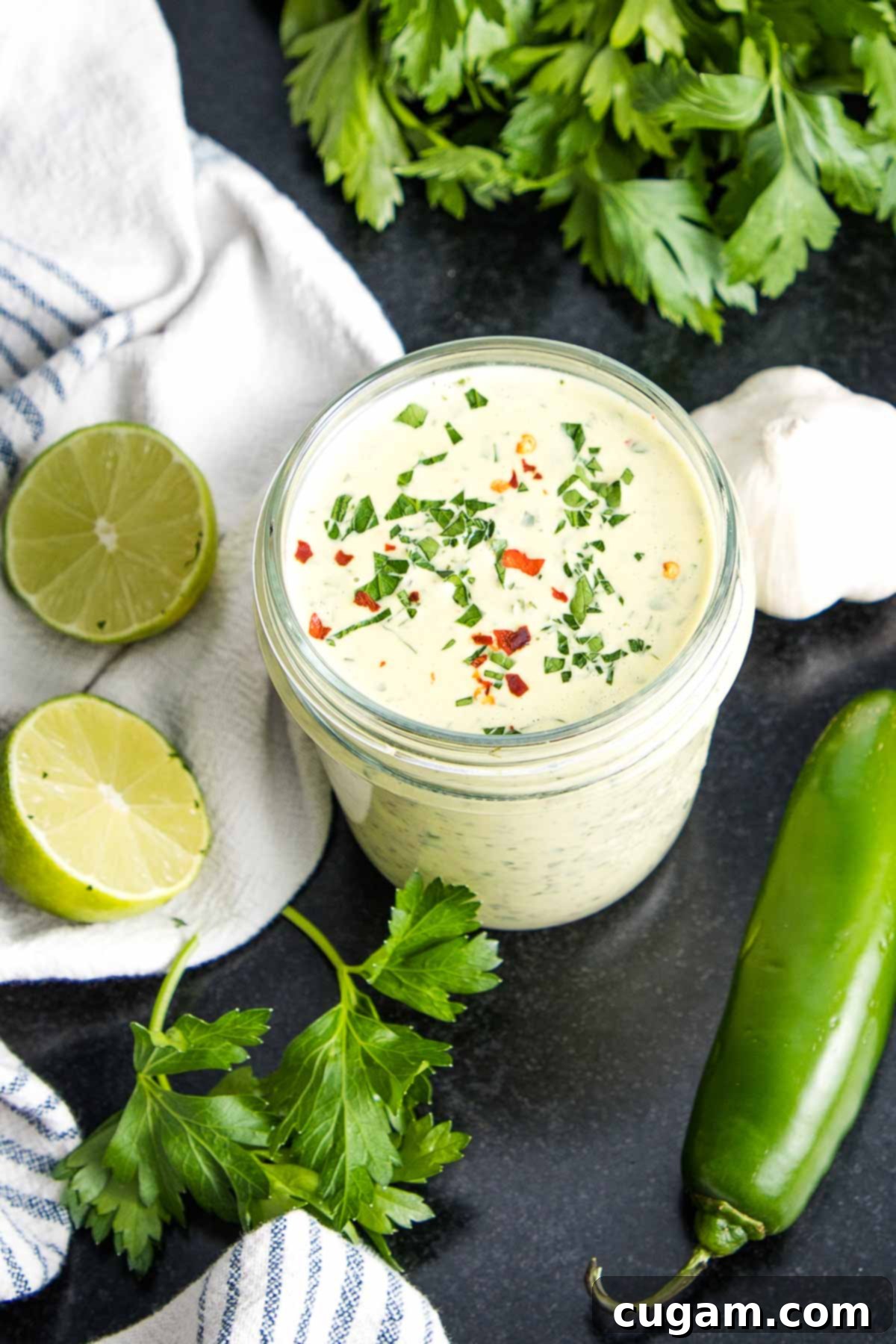 Green tahini sauce in a mason jar with specks of fresh herbs and crushed red pepper, ready to be served or stored.