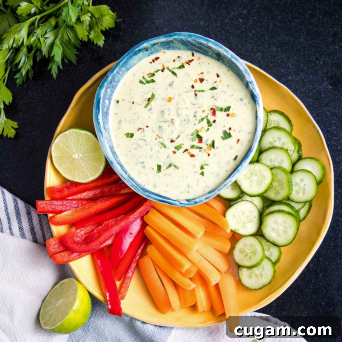 Green tahini sauce served in a small white bowl, elegantly arranged on a plate with an assortment of crisp sliced bell peppers, carrots, and cucumbers for dipping.