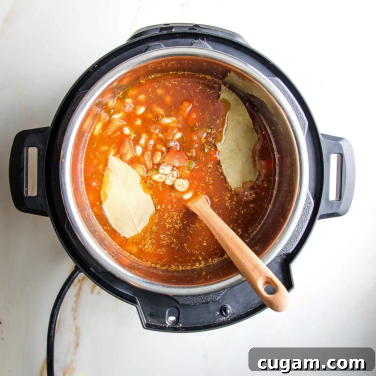 Instant pot filled with tomato sauce, spices, bay leaves and veggies.