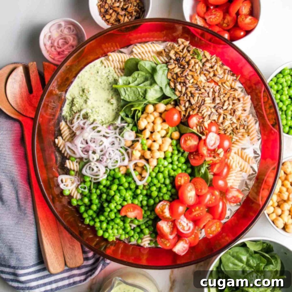 Simple Summer Pasta Salad 4 Large bowl with red rim, generously filled with corkscrew pasta, bright red halved cherry tomatoes, green peas, chickpeas, a drizzle of green tahini dressing, and a sprinkling of sunflower seeds.