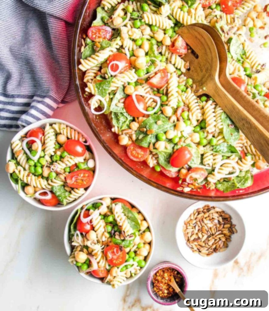 Simple Summer Pasta Salad 5 Serving colorful pasta salad from a large red glass bowl into smaller white bowls, with extra sunflower seeds and red pepper flakes available for garnish.