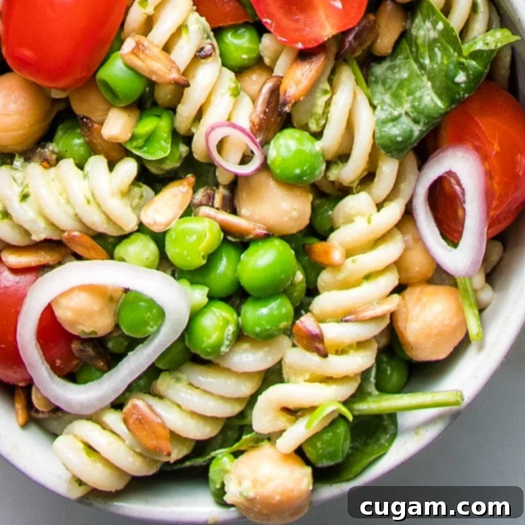 Simple Summer Pasta Salad 6 Close-up view of corkscrew pasta tossed with thinly sliced shallot rings, bright green peas, chickpeas, halved cherry tomatoes, fresh spinach, and sunflower seeds.