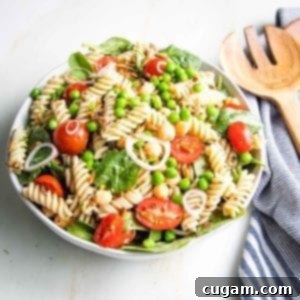 Simple Summer Pasta Salad 7 Large white bowl filled with cherry tomatoes, fusilli pasta, green peas, chick peas, sunflower seeds with a striped blue napkin on the side.