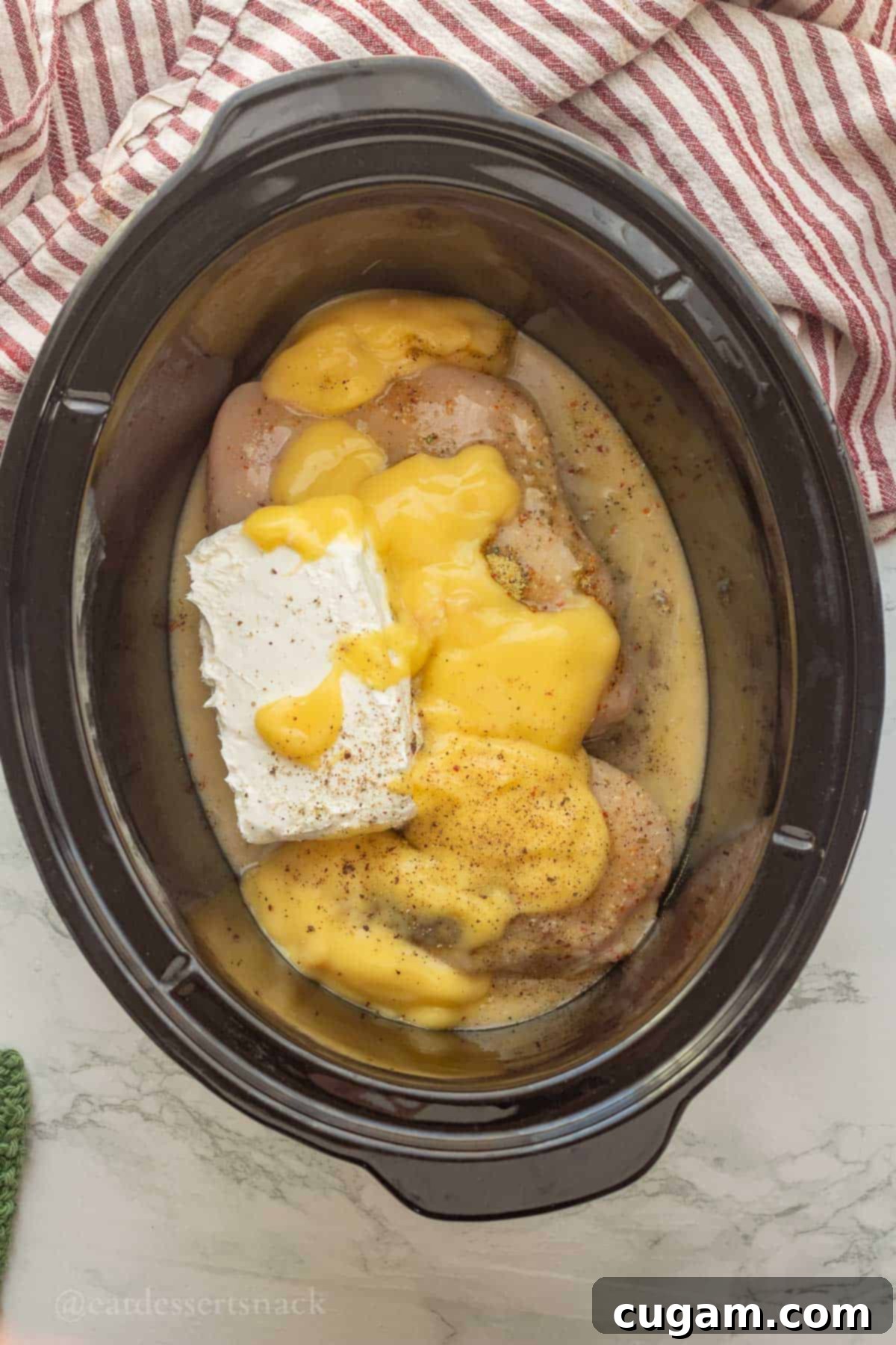 Cream cheese, condensed cream of chicken soup, italian dressing, and raw chicken in black crockpot.