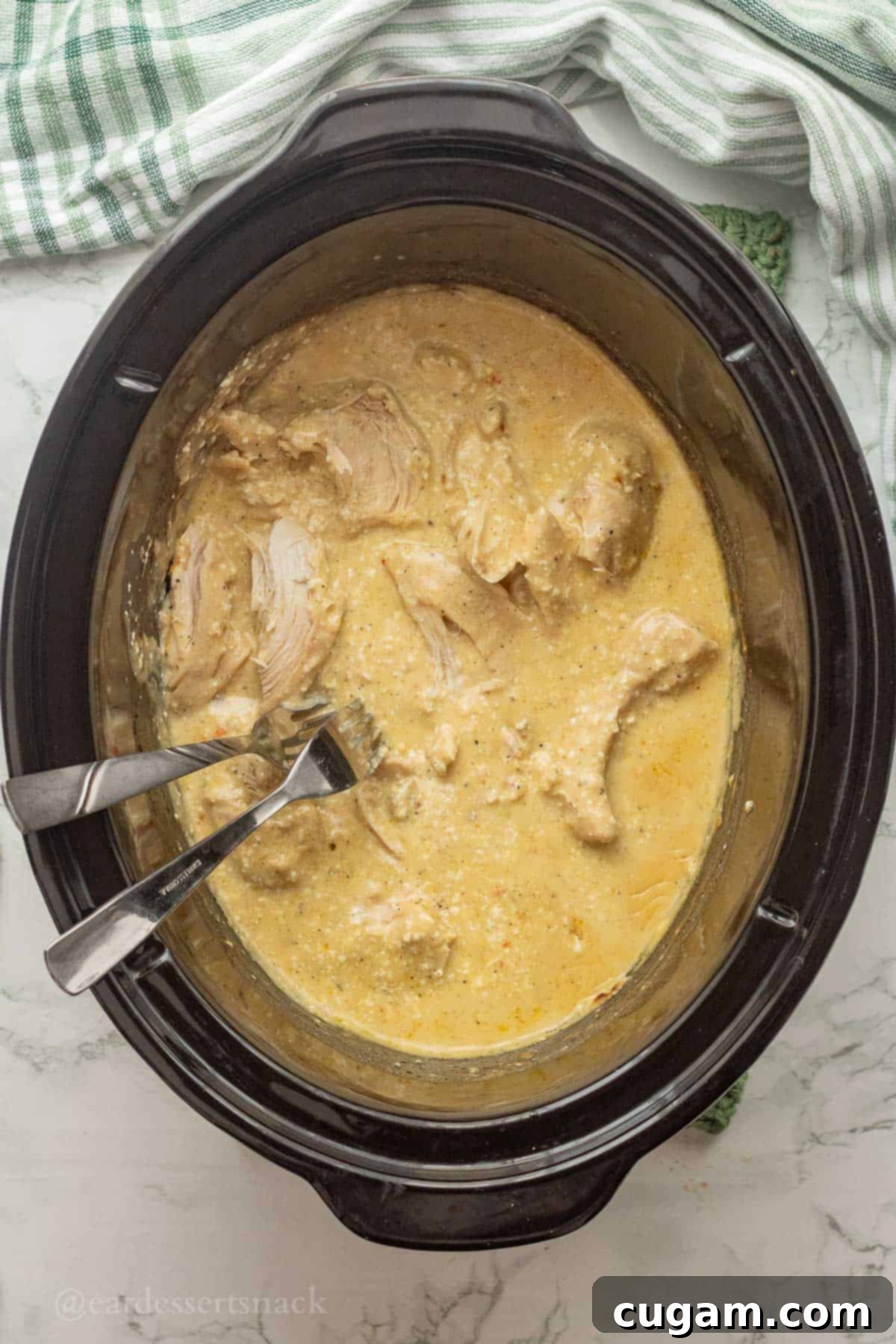 Two forks shredding cooked italian chicken in crockpot.