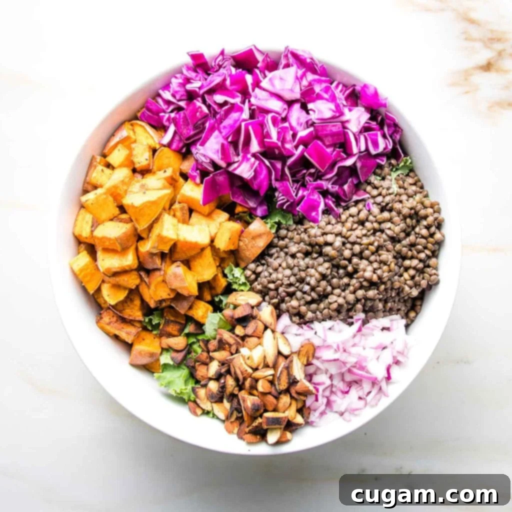 A mix of roasted sweet potato cubes, coarsely chopped purple cabbage, cooked black lentils, diced red onion, and toasted almonds in a white bowl.