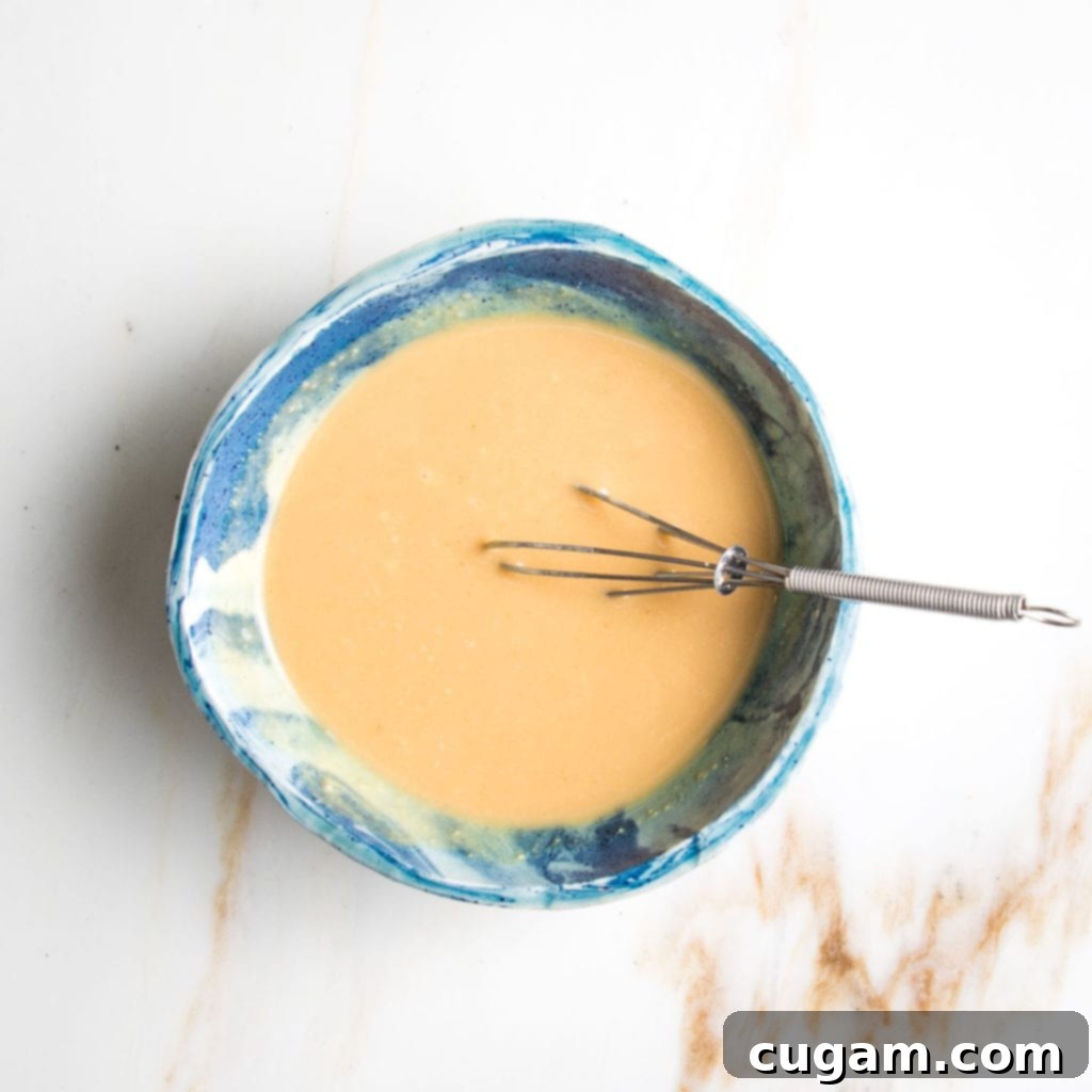A simple yet elegant miso mustard dressing in a bright blue bowl, accompanied by a small whisk, ready to be emulsified.