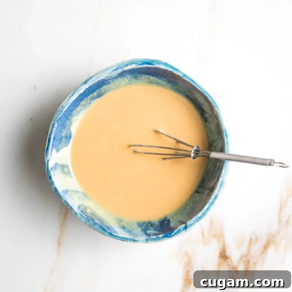 Simple oil-free miso mustard dressing being whisked in a bright blue bowl.