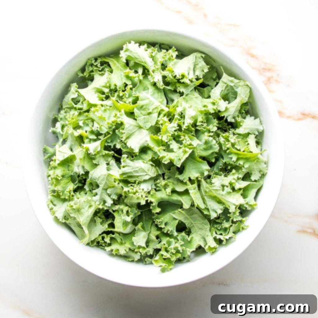 A large white bowl generously filled with curly green kale, prepared and ready for the other salad ingredients.