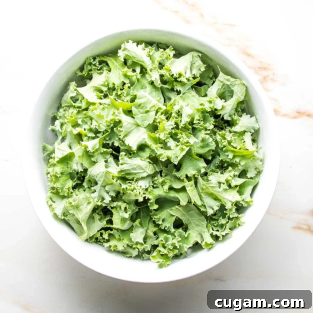 Large white bowl brimming with fresh, curly green kale leaves.