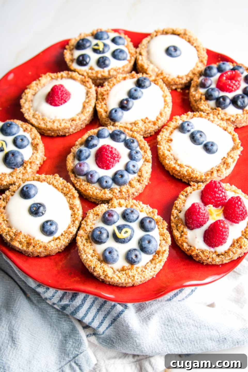 A bright red cake stand elegantly displaying an assortment of mini berry tarts, beautifully decorated with a mix of fresh raspberries and blueberries.