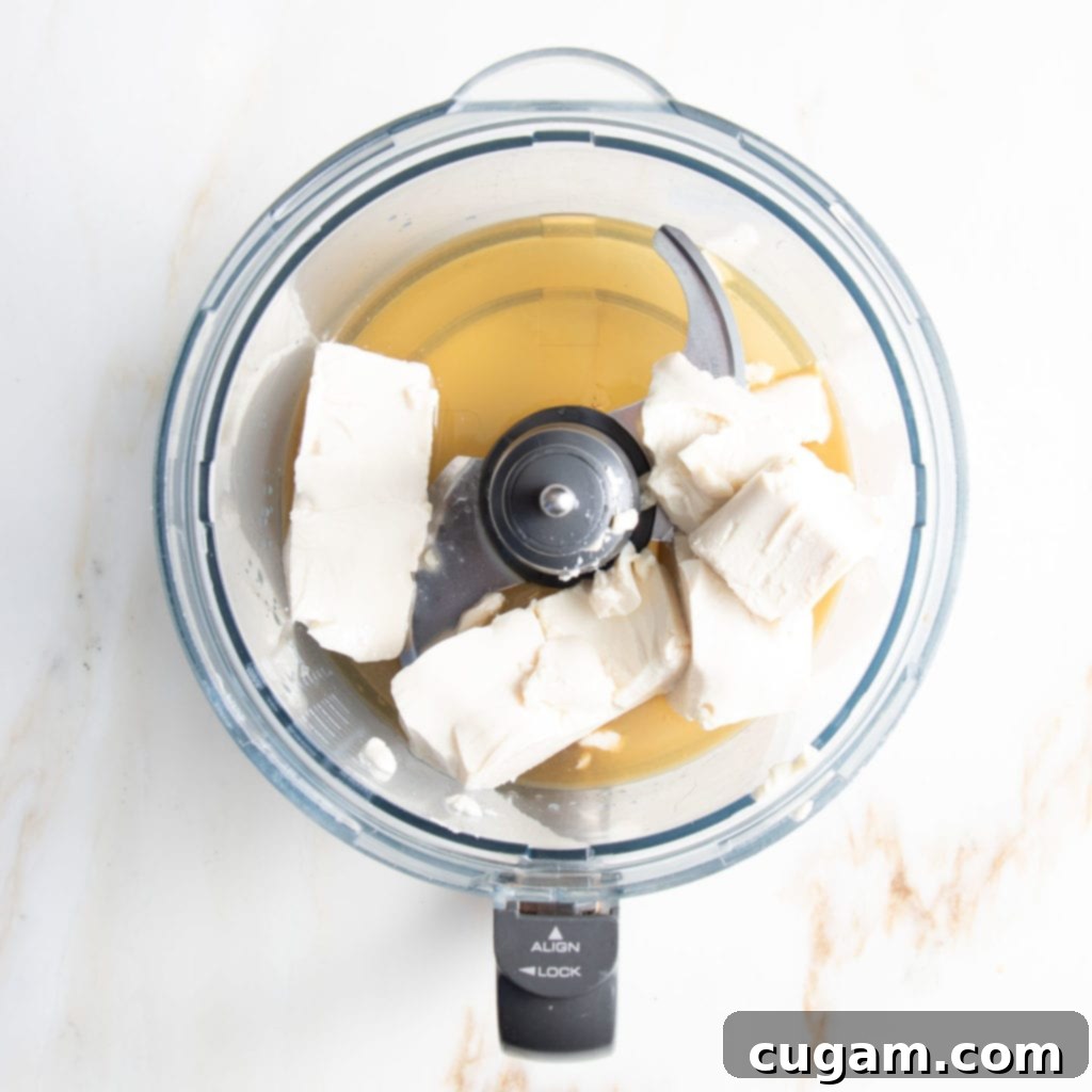A food processor bowl filled with the ingredients for the creamy vegan tart filling: silken tofu, maple syrup, fresh lemon juice, and vanilla extract. Ready to be processed for a healthy blueberry tart.
