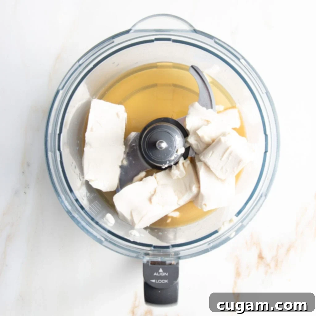 Food processor bowl filled with tofu, maple syrup, lemon juice and vanilla extract....ready to process into a creamy vegan filling for healthy blueberry tart. 