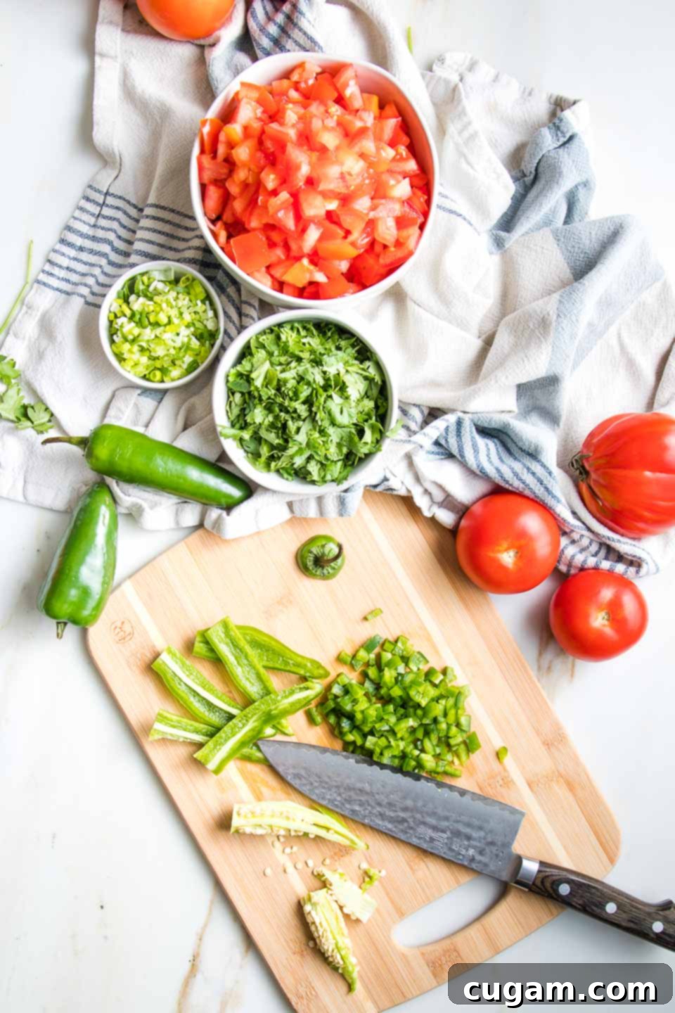 Fresh chopped tomatoes, cilantro and scallion for salsa, along with a cutting board with knife, showing how to remove the seeds and membranes from the jalapeno to chop.