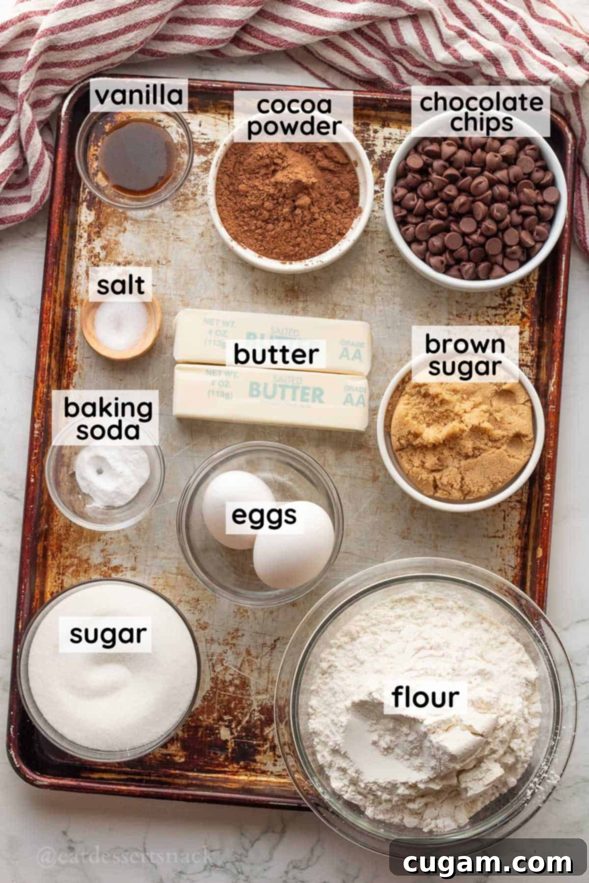 Labeled ingredients for chocolate chocolate chip cookie bars on metal baking sheet.