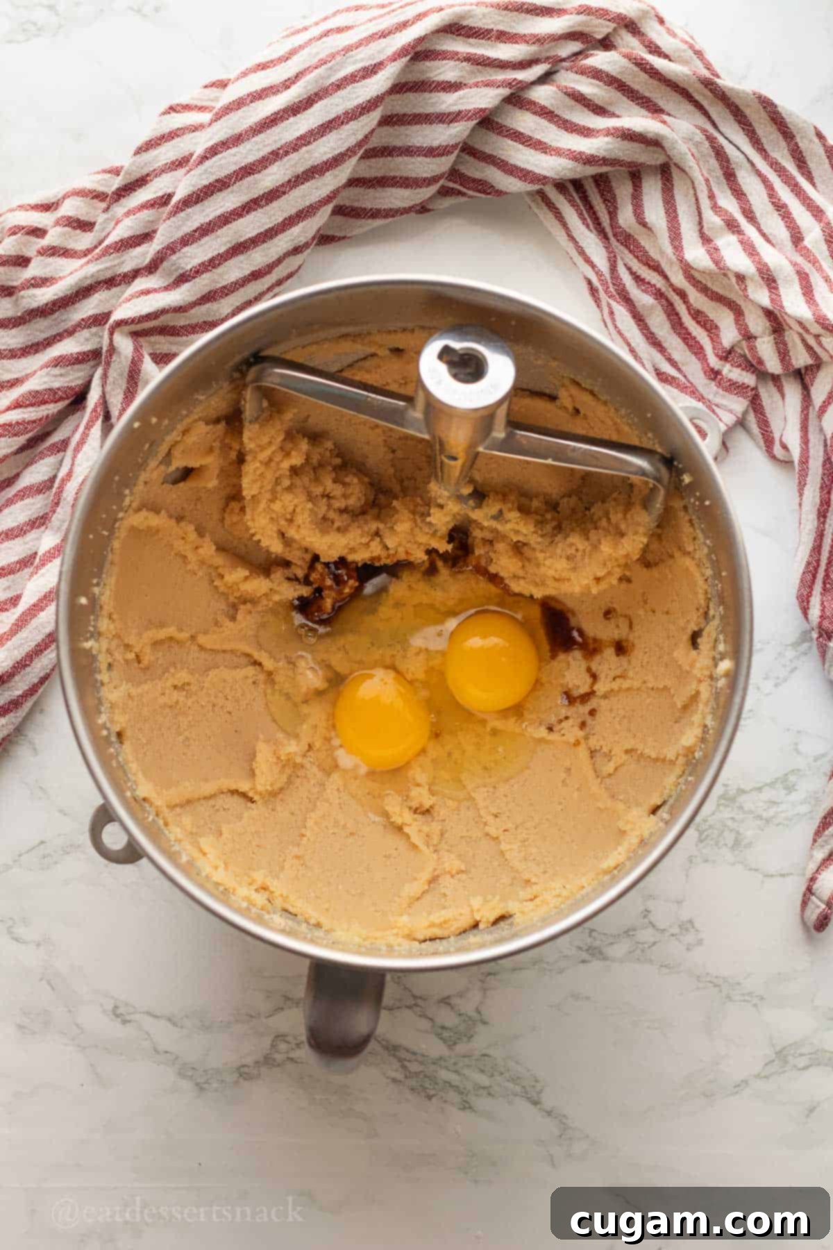 Eggs and vanilla in metal mixing bowl with butter and sugar.