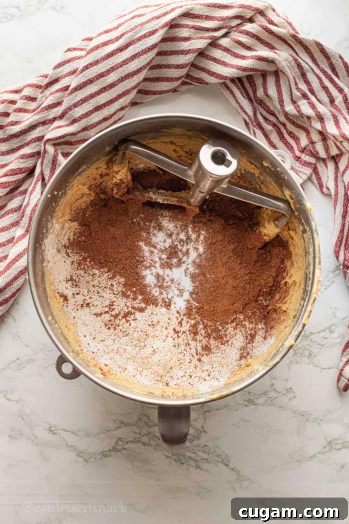 Flour and cocoa powder in metal mixing bowl with cookie batter.
