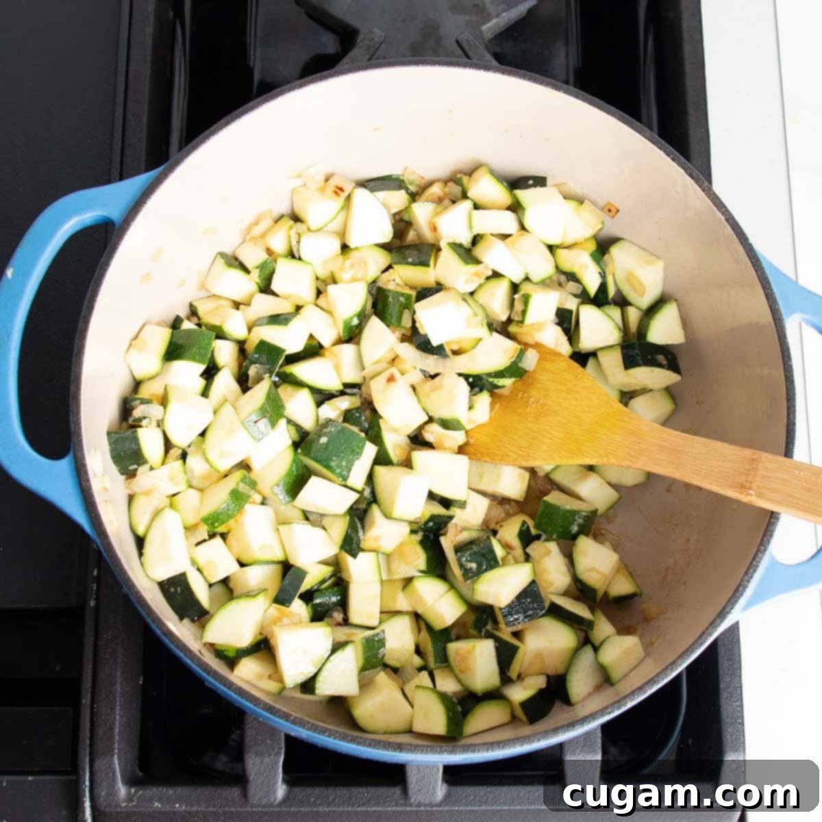 Easy Creamy Zucchini Soup 7 Dutch oven with chopped zucchini, onions, garlic and a wooden spoon stirring.