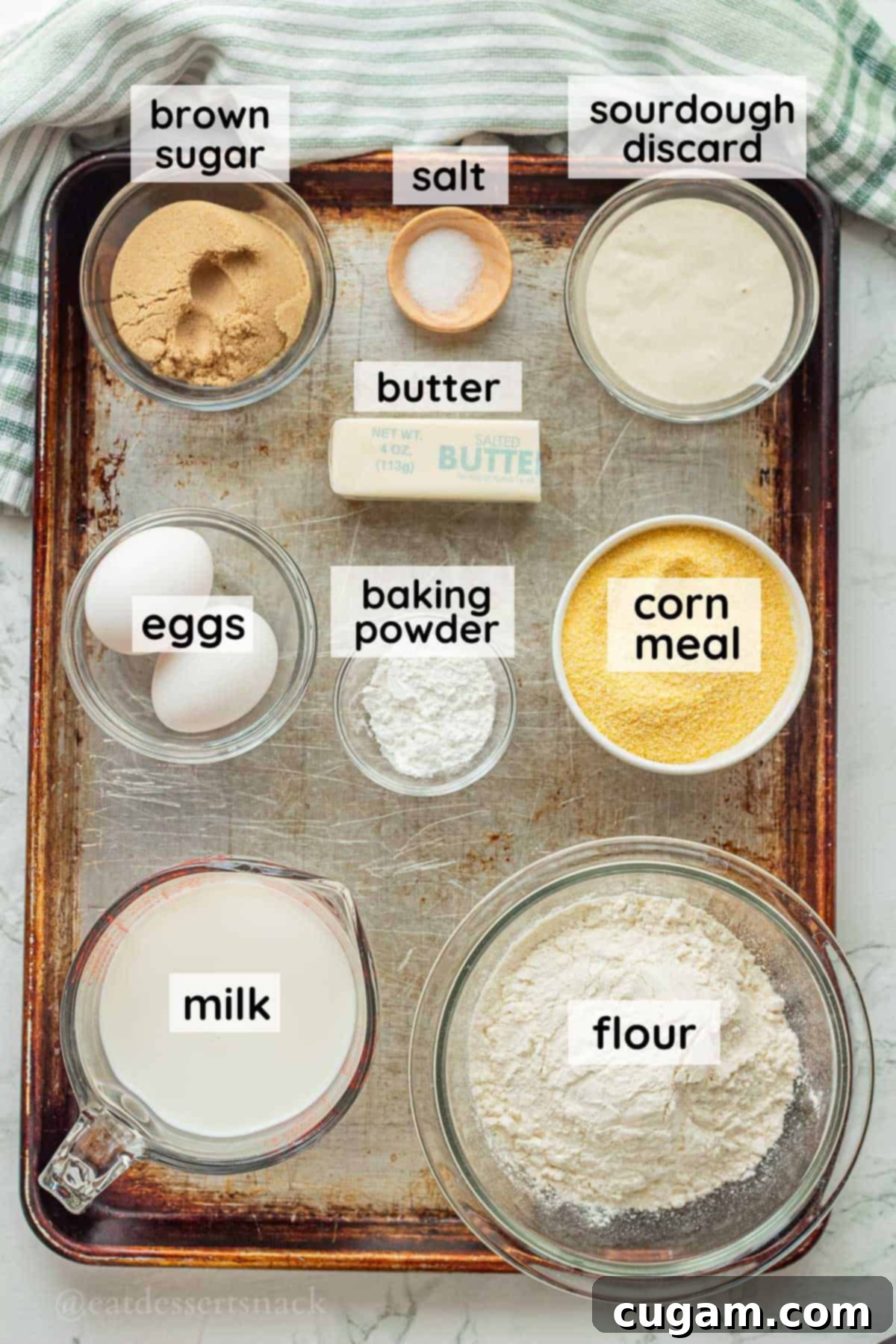 Labeled ingredients for sourdough discard cornbread laid out on a metal baking sheet in glass dishes.