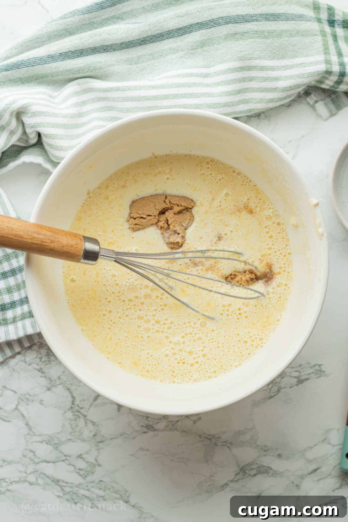 Brown sugar being added to the wet ingredients in a white bowl, ready for mixing.