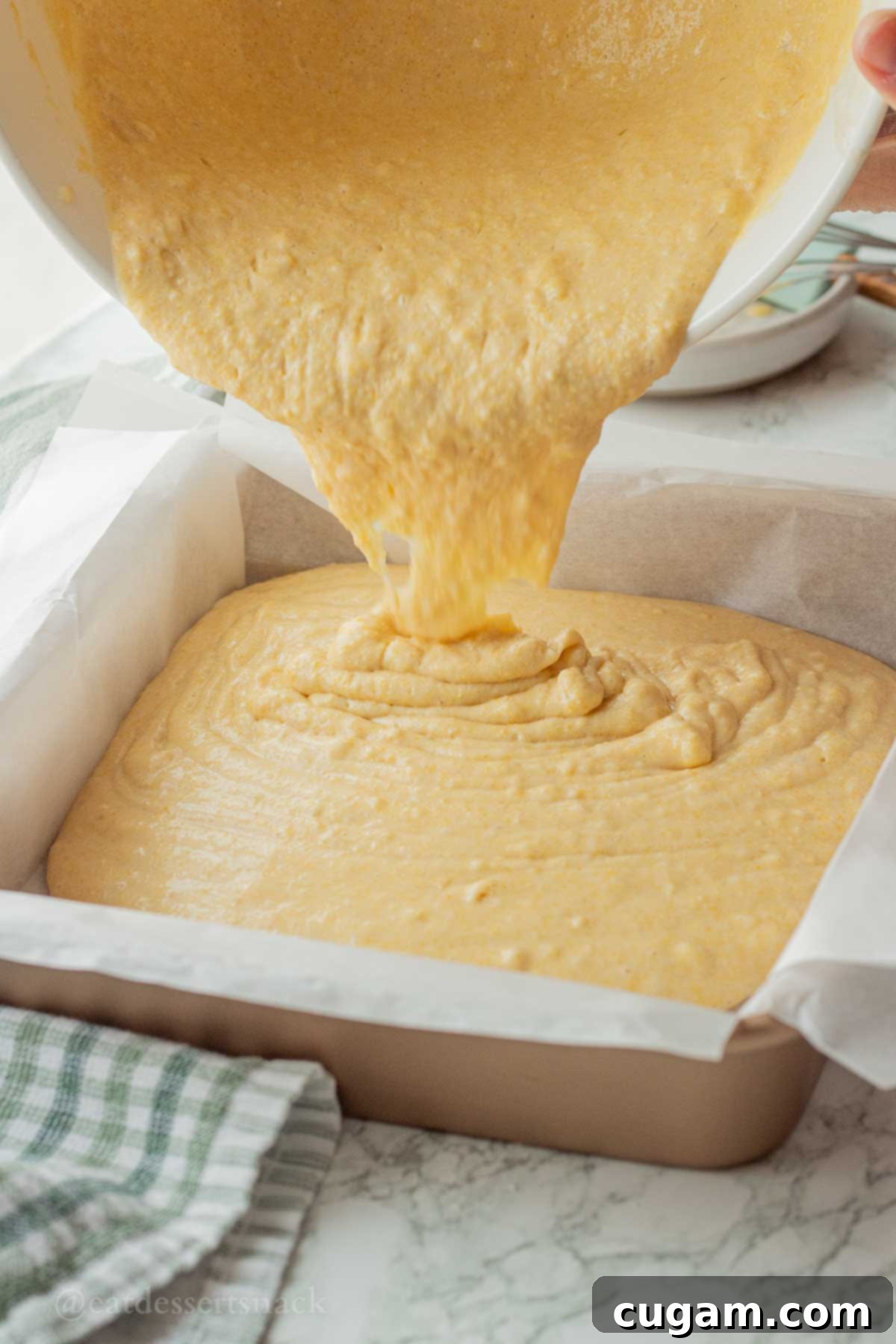 Pouring raw cornbread batter into a prepared metal baking dish.