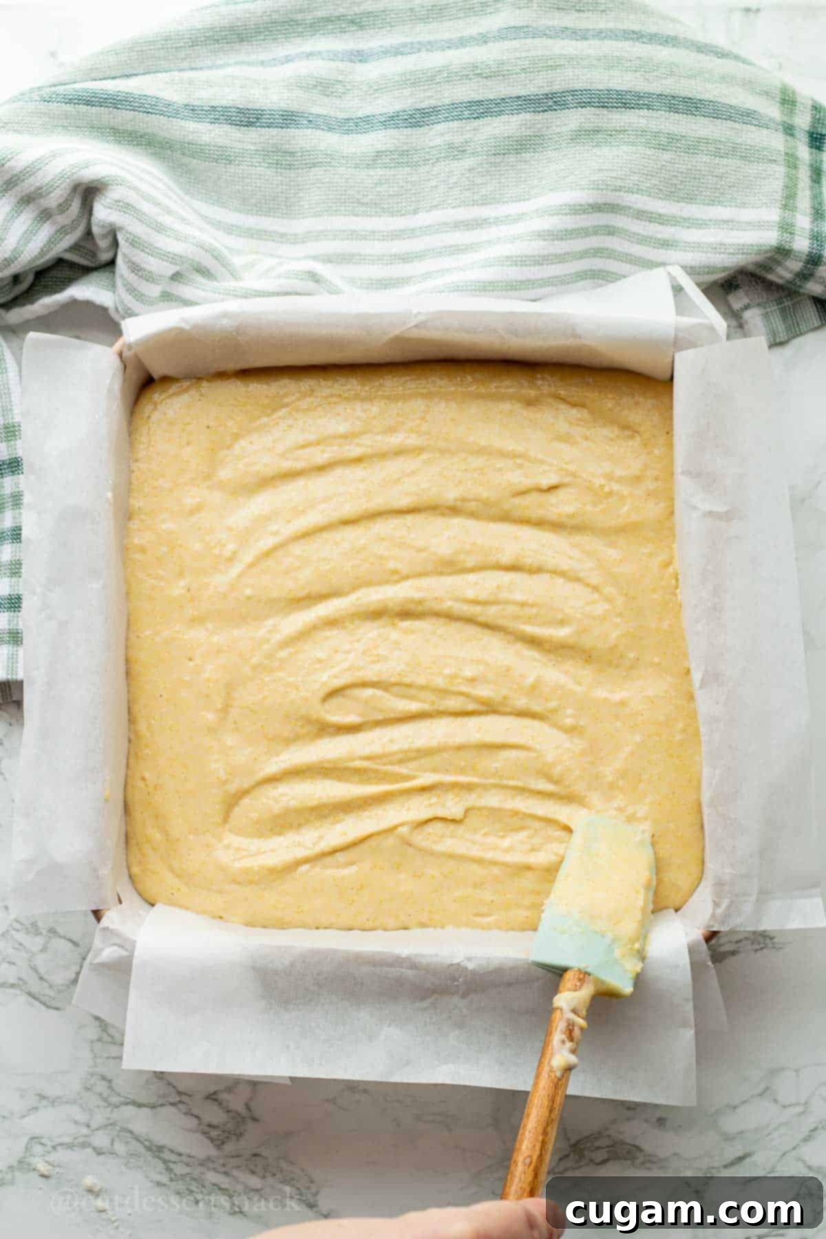 Smoothing out raw cornbread batter in a baking dish with a spatula before baking.