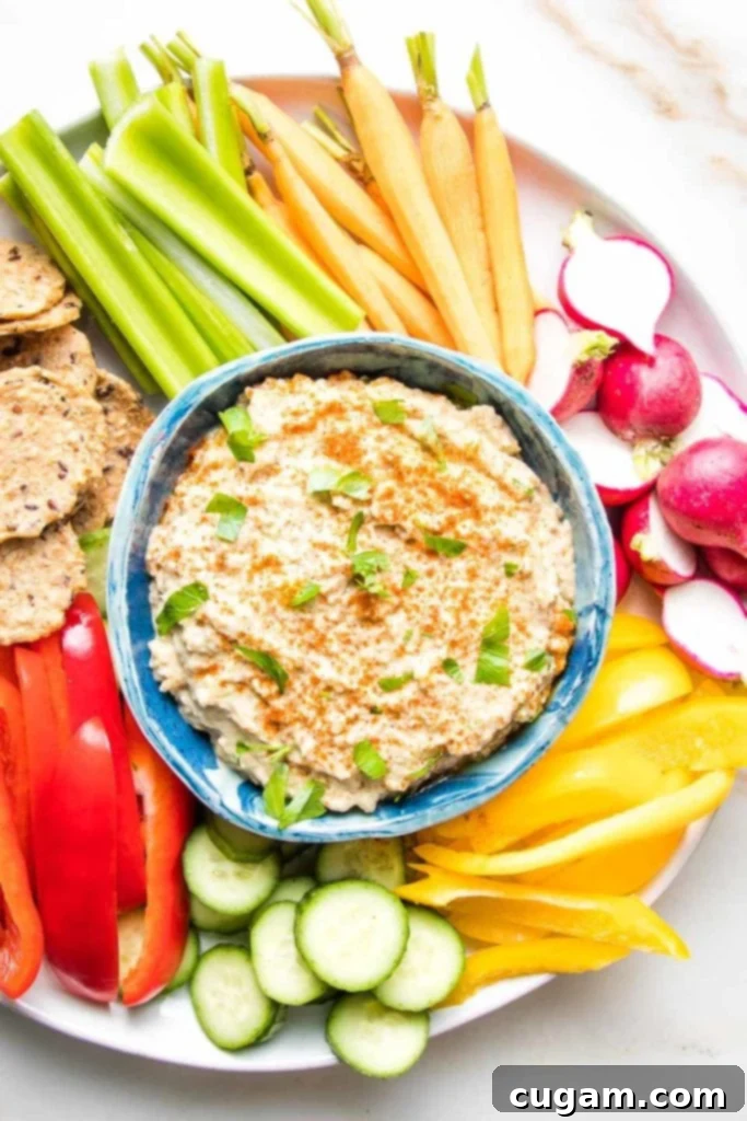 Baba Ganoush in a blue bowl sprinkled with paprika and fresh parsley with crudites of brightly colored radish, bell peppers, celery, carrots and crackers.