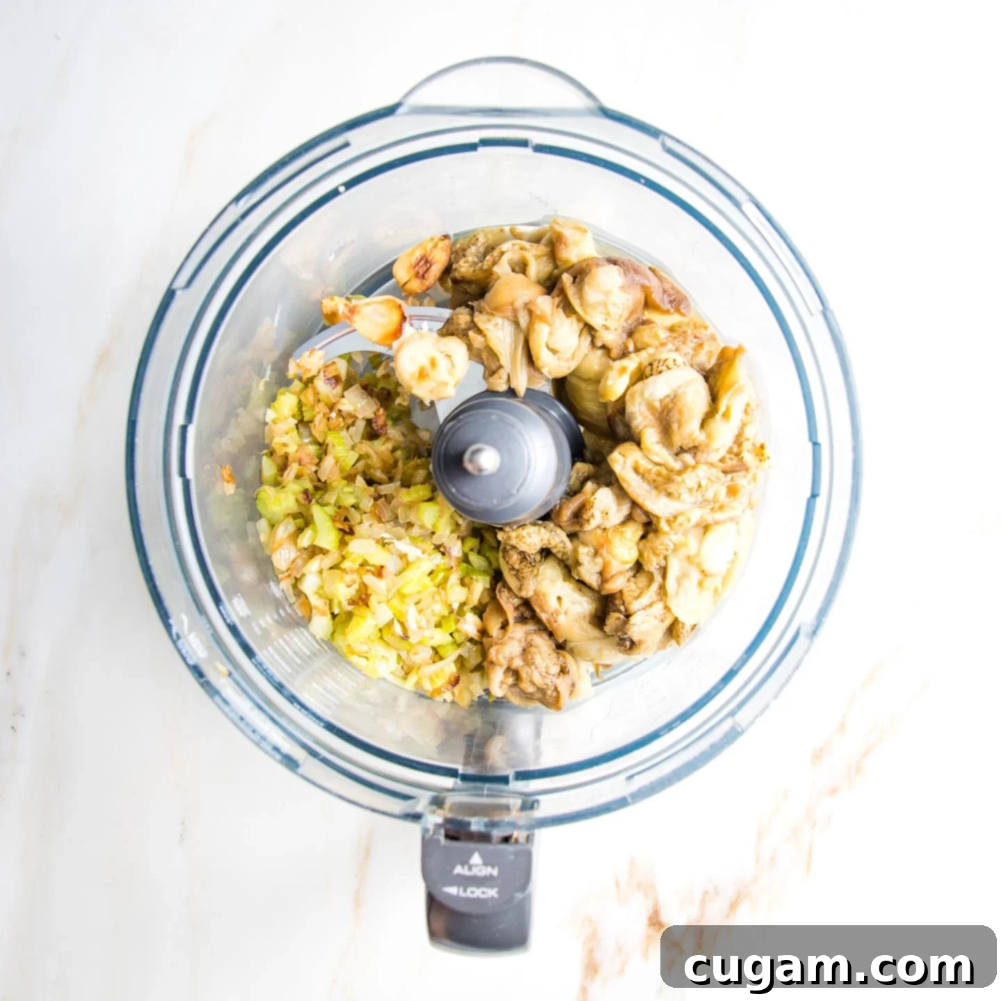 Chunks of roasted eggplant and garlic plus sauteed veggies in the bowl of a food processor.