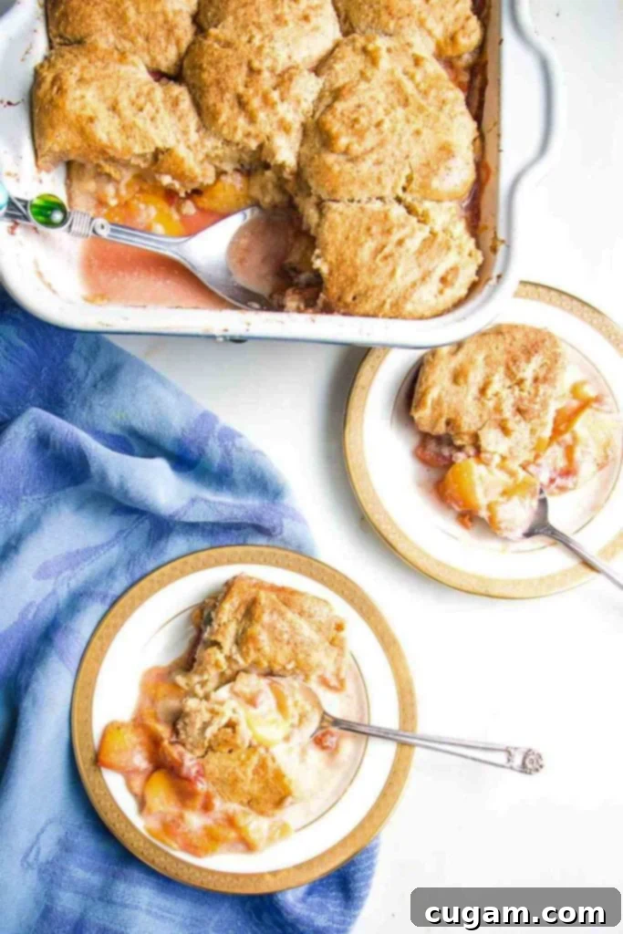 Baking dish of peach cobbler and two servings on plates with spoons.