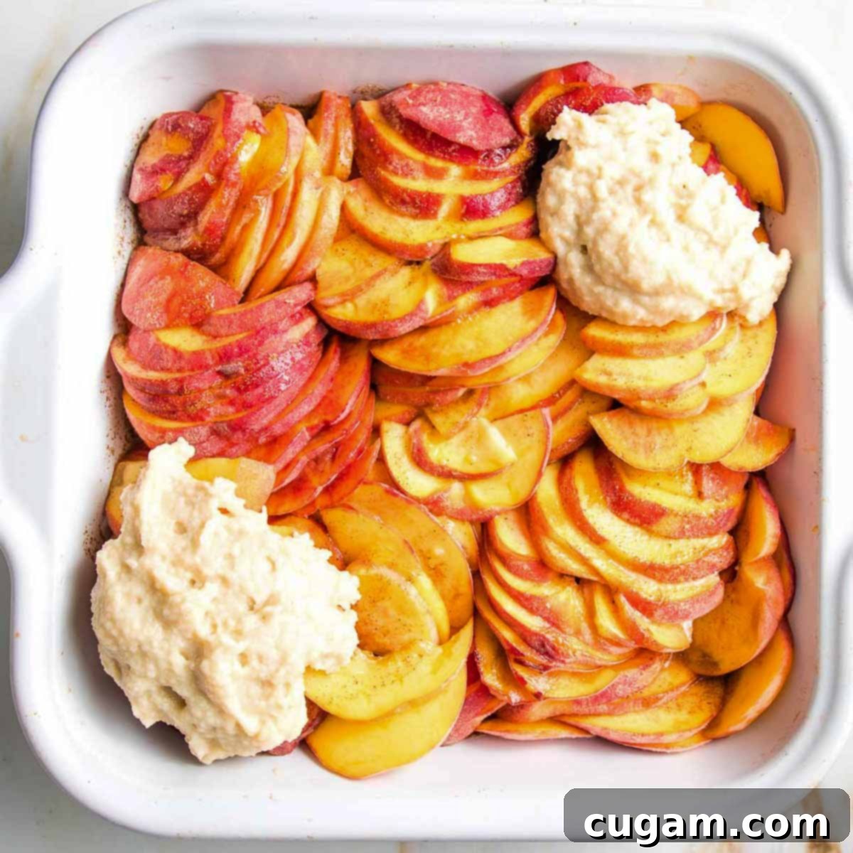 Sliced peaches with a couple dollops of cobbler topping in a square baking dish.