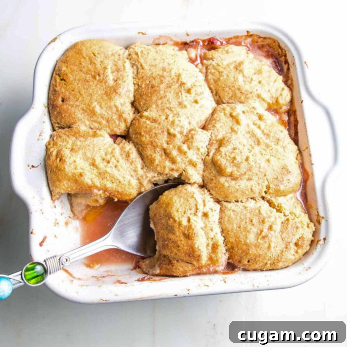 A baking dish of golden-brown peach cobbler fresh out of the oven, steam rising from the delicious topping.