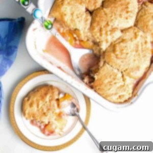 Serving of peach cobbler on a china plate with baking dish in the background.