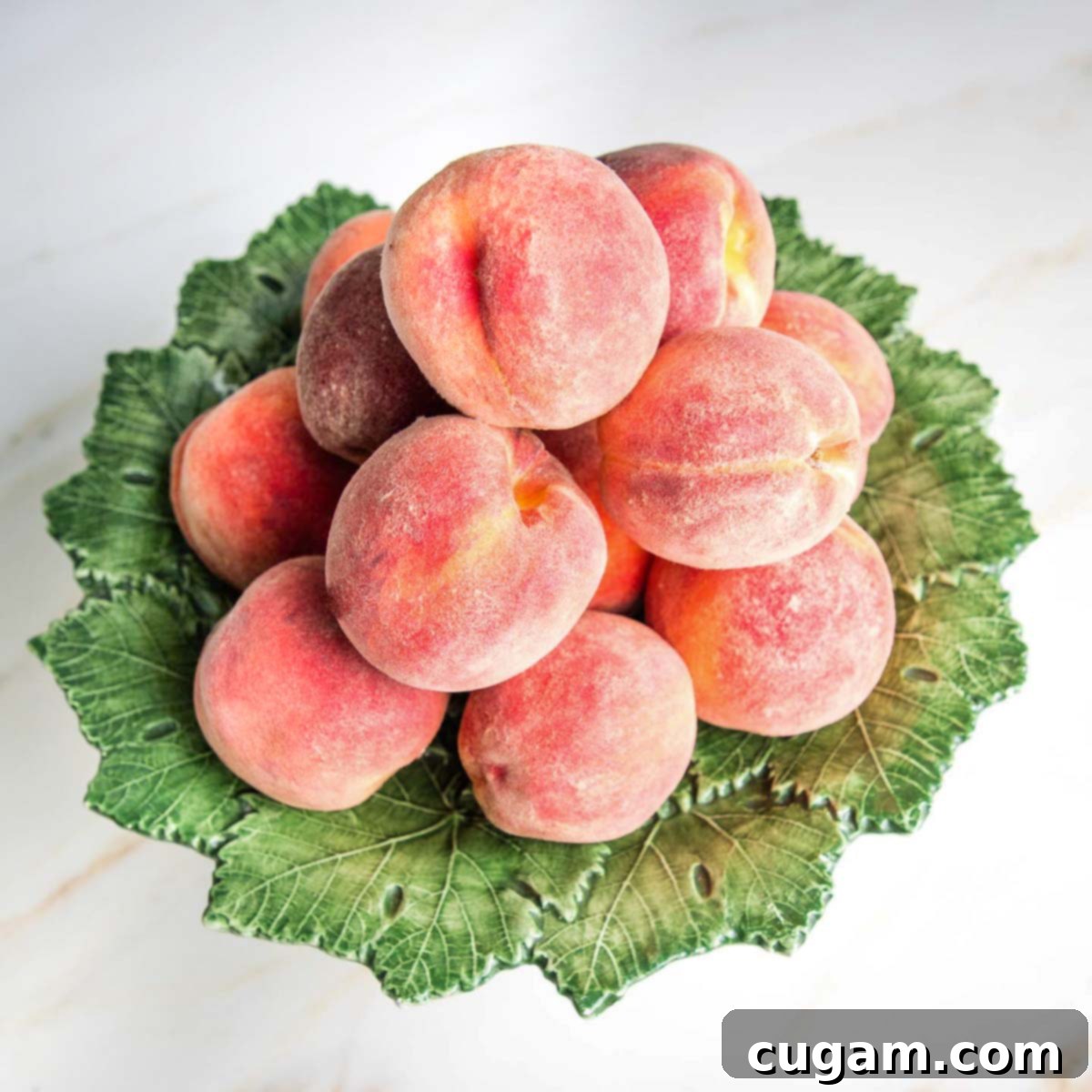 Pile of fresh peaches on a green leafy pedestal.