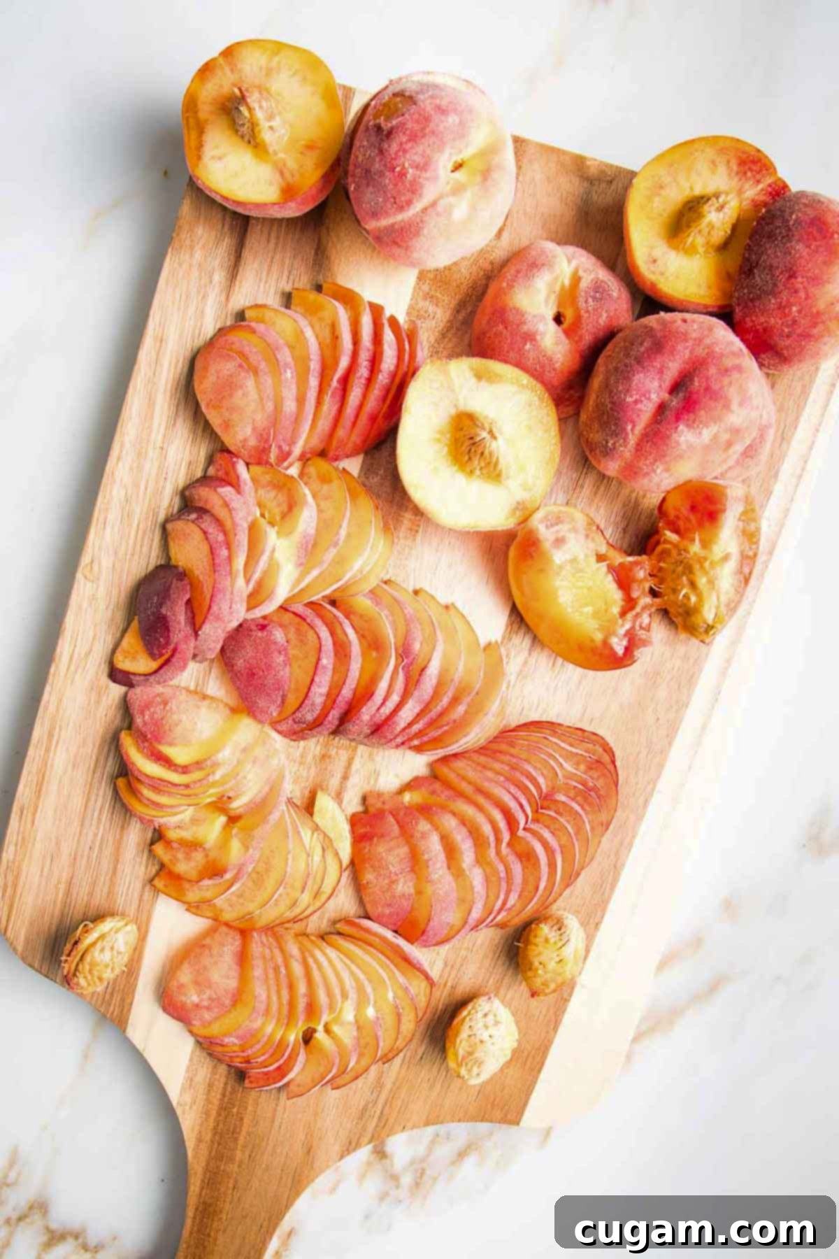 Cutting board filled with halved peaches, some sliced thin, some with pits removed.