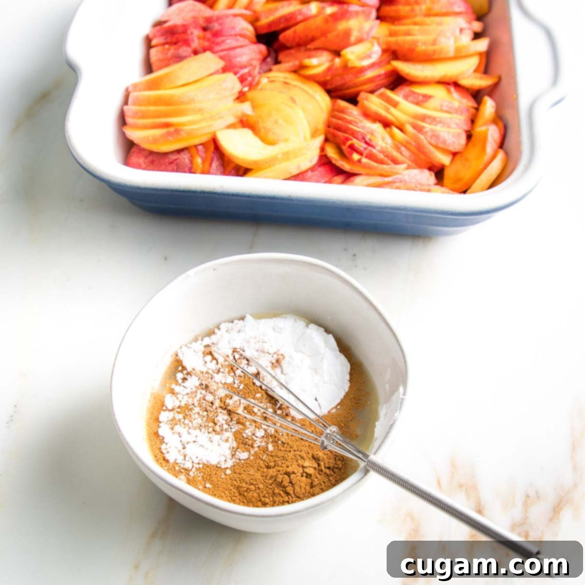 Bowl of arrowroot powder, cinnamon, lemon juice in front of a baking dish filled with peach slices.