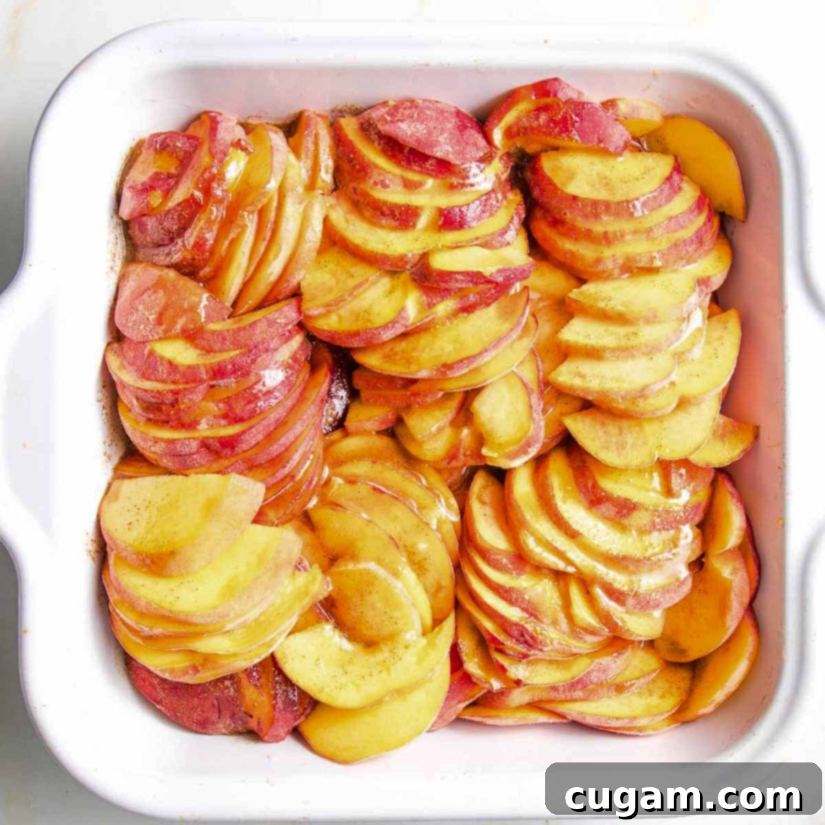 Baking dish filled with peach slices, covered with jammy lemony cinnamon. 