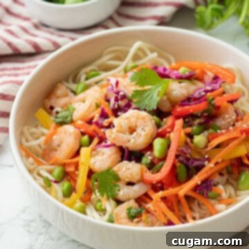Chopped veggies in white bowl with cooked shrimp over bed of noodles.