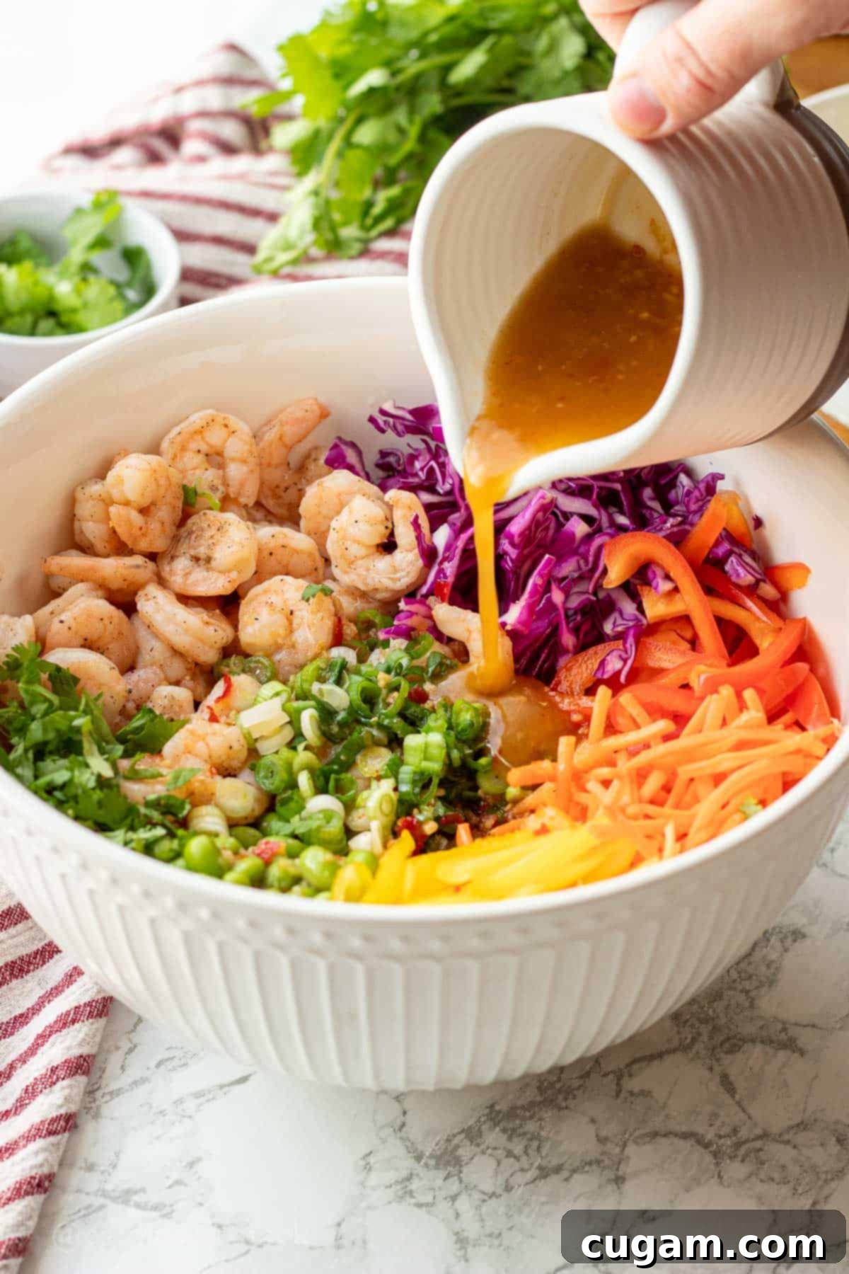 Pouring ginger lime dressing into white bowl of chopped veggies and cooked shrimp.