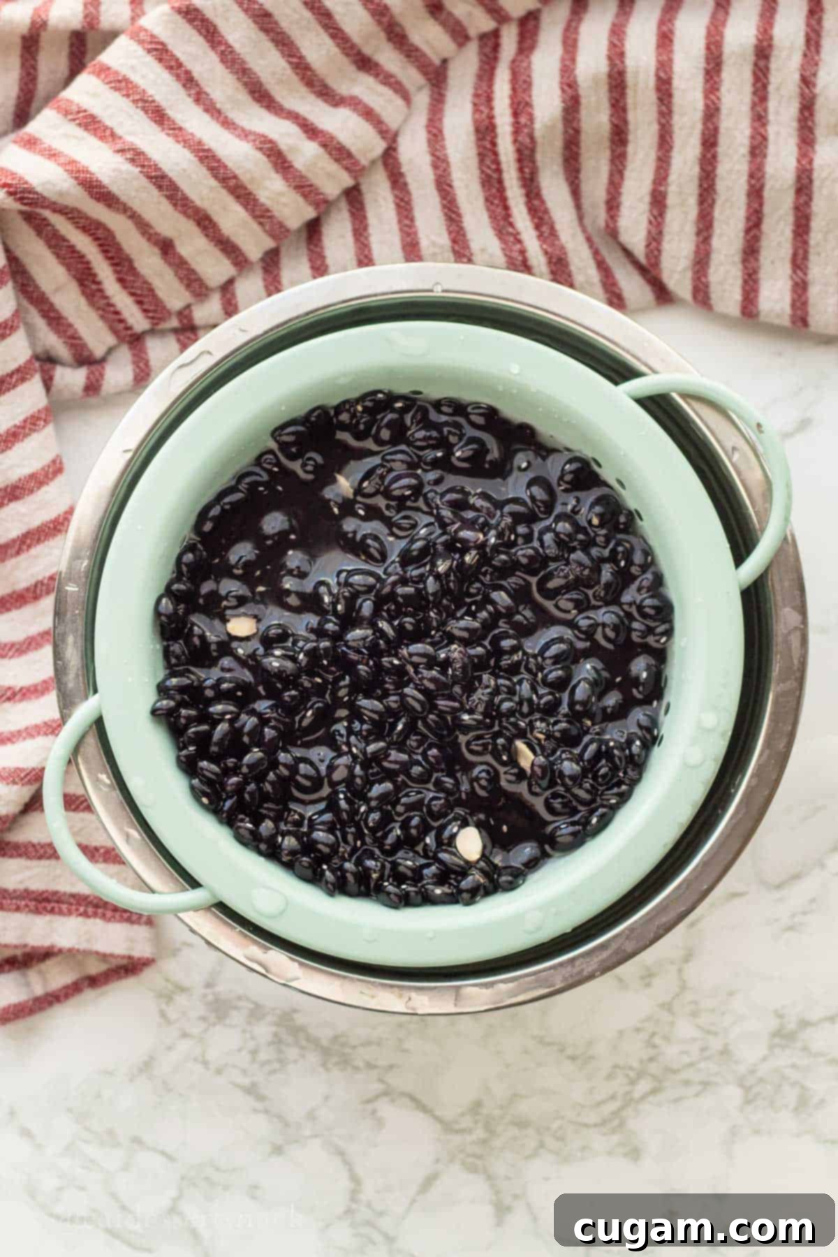 Colander full of uncooked black beans in bowl of water.