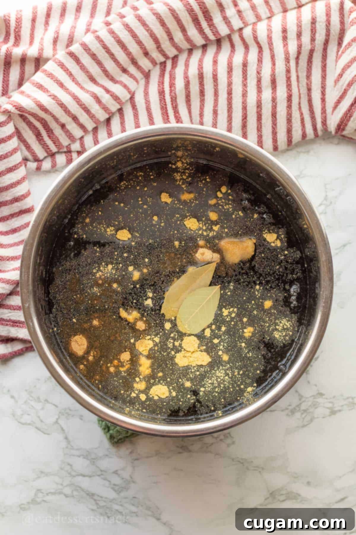 Spices and bay leaves in water with uncooked black beans in metal pot.