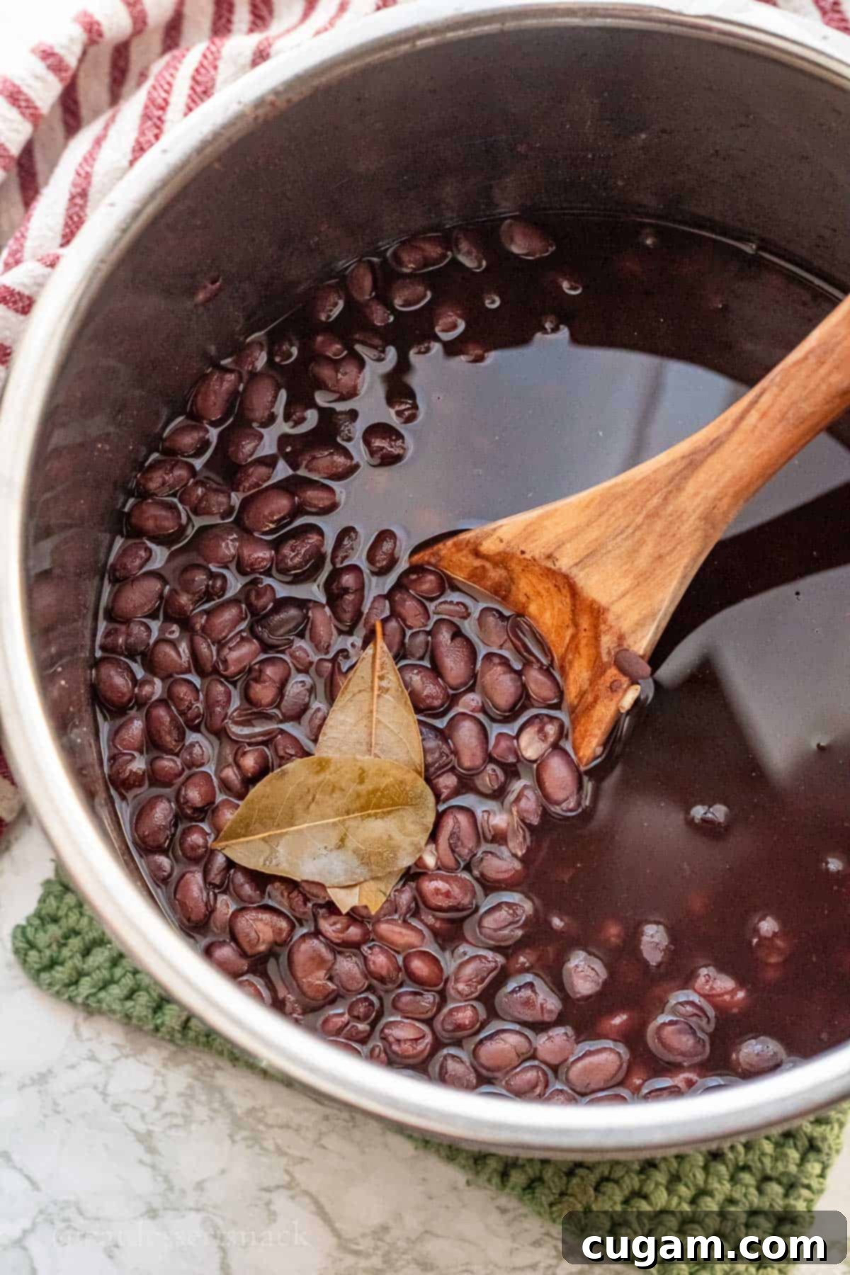 Cooked black beans with wooden spoon and bay leaves in metal pot.